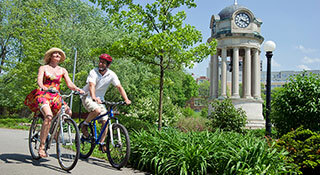 Women and man biking through Victoria Part with a clock tower in the background